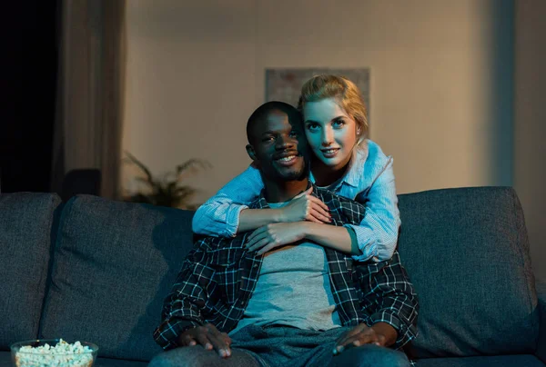 Портрет многонациональной пары, смотрящей телевизор вместе на диване дома — стоковое фото