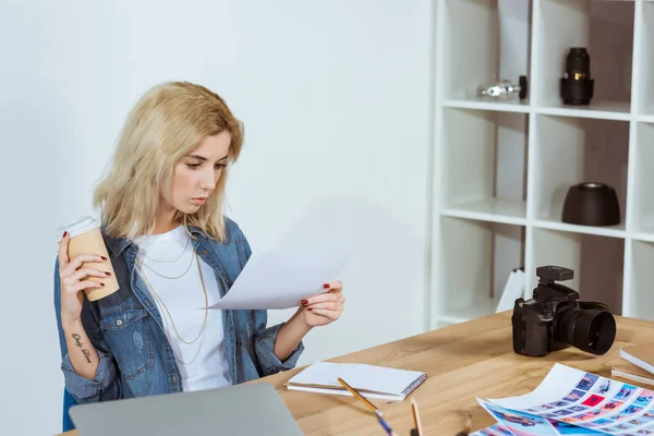 Photographer with coffee to go looking at photoshoot samples at workplace in office — Stock Photo