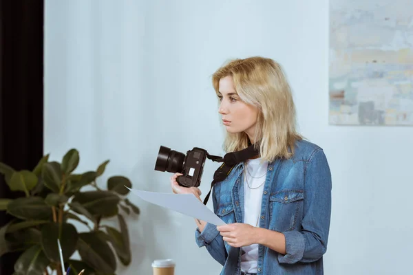 Side view of thoughtful photographer with photo camera and photoshoot example looking away in studio — Stock Photo