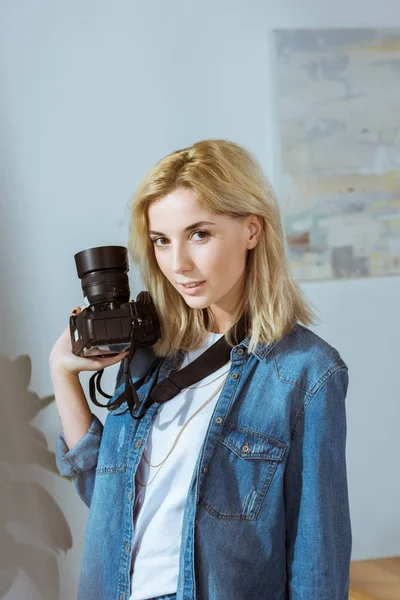 Porträt eines lächelnden Fotografen mit einer Fotokamera in der Hand, die auf die Kamera im Studio blickt — Stockfoto