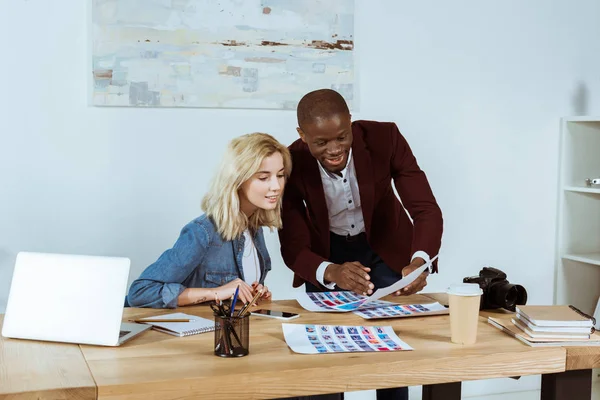 Portrait of multiethnic photographers looking at portfolio at workplace in office — Stock Photo