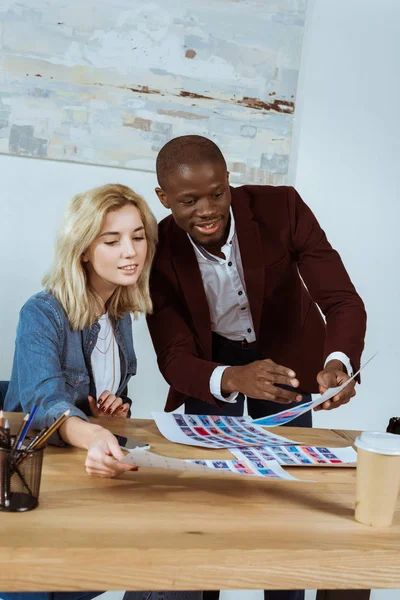 Portrait of multiethnic young photographers looking at portfolio at workplace in office — Stock Photo