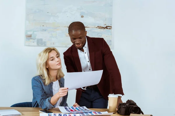 Fotógrafos multiculturais escolhendo portfólio juntos no local de trabalho no escritório — Fotografia de Stock