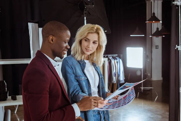 Portrait of multiethnic photographers looking at portfolio together in studio — Stock Photo