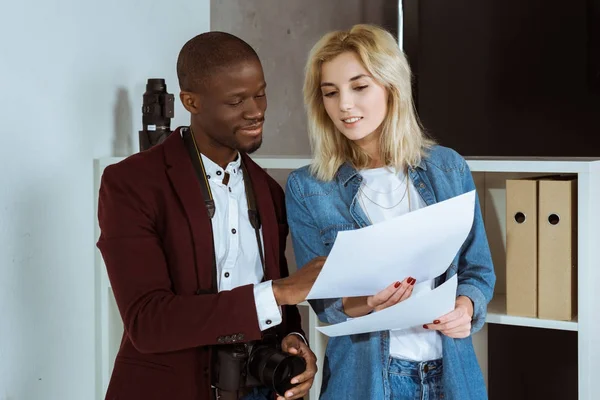 Portrait of multiethnic photographers looking at portfolio together in studio — Stock Photo