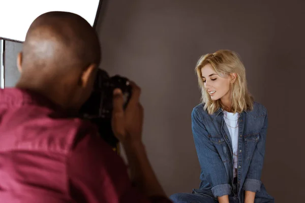 Beautiful smiling caucasian woman posing while african american photographer taking picture in studio — Stock Photo