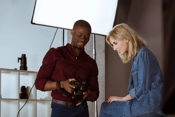 Photographe afro-américain et modèle caucasien choisissant des photos ensemble pendant la séance photo en studio — Photo de stock