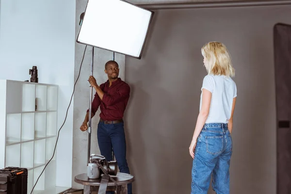 Fotógrafo afro-americano corrigindo a luz antes da sessão fotográfica em estúdio — Fotografia de Stock