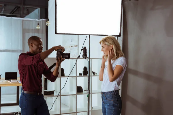 Fotografo afroamericano che scatta foto di attraente modella in studio — Foto stock