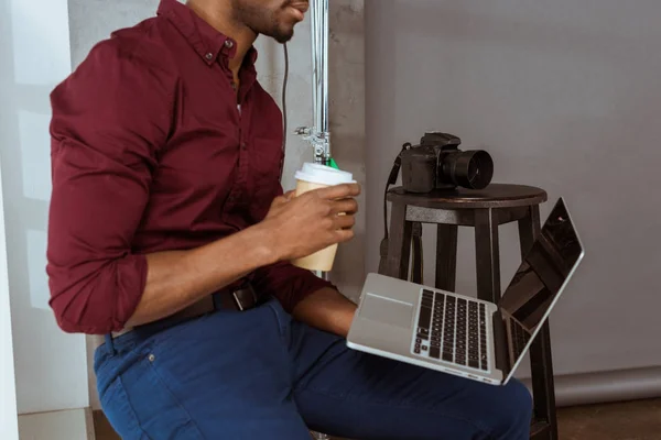 Plan recadré du photographe afro-américain avec café pour aller travailler sur ordinateur portable en studio — Photo de stock