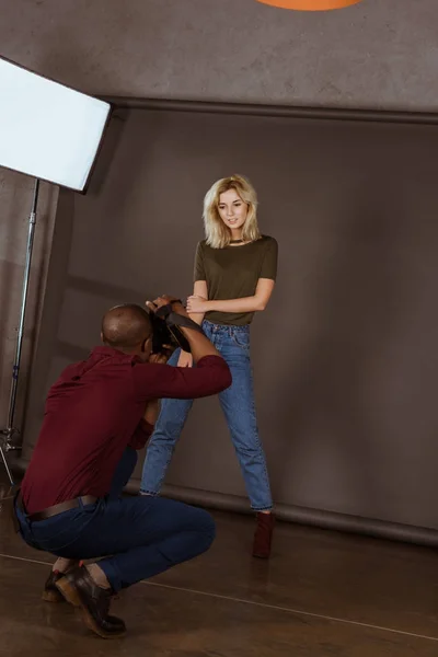 Hermosa mujer caucásica posando mientras que el fotógrafo afroamericano tomando foto en el estudio - foto de stock