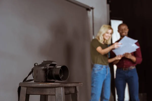 Foco seletivo da câmera fotográfica e fotógrafo e modelo afro-americano olhando para o portfólio em estúdio — Fotografia de Stock