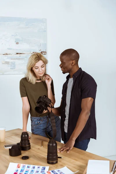 Interracial photographers talking about photo cameras at workplace in studio — Stock Photo