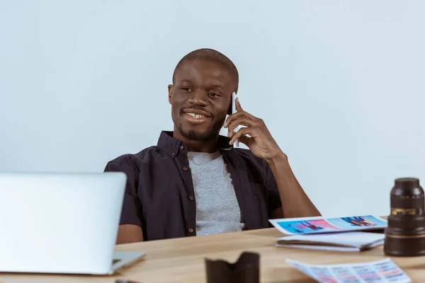Портрет улыбающегося африканского фотографа, разговаривающего по смартфону на рабочем месте в студии — стоковое фото