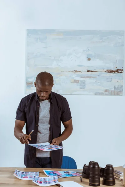 Retrato de fotógrafo afro-americano focado olhando para exemplos de fotos em mãos enquanto estava no local de trabalho — Fotografia de Stock