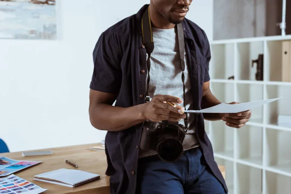 Scatto ritagliato di fotografo afroamericano con esempi di photoshoot in mano sul posto di lavoro — Foto stock