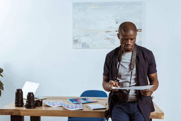 Portrait of african american photographer looking at photoshoot examples in hands at workplace — Stock Photo