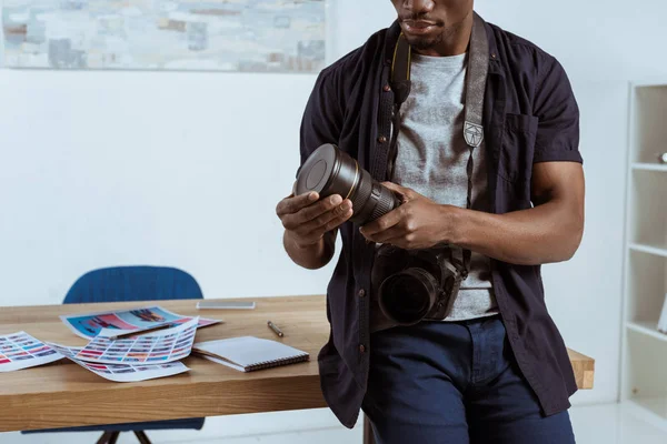 Teilbild eines afrikanisch-amerikanischen Fotografen mit Fotokamera am Arbeitsplatz im Büro angelehnt — Stockfoto