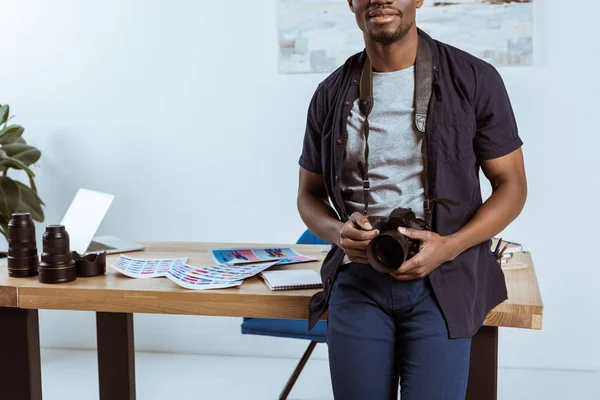 Vue partielle du photographe afro-américain avec appareil photo penché sur le lieu de travail au bureau — Photo de stock