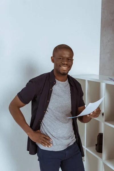 Retrato del alegre hombre afroamericano con papeles en la mano mirando la cámara en el estudio - foto de stock