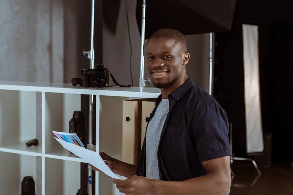 Porträt eines fröhlichen afrikanisch-amerikanischen Mannes mit Papieren in der Hand, der im Studio in die Kamera blickt — Stockfoto
