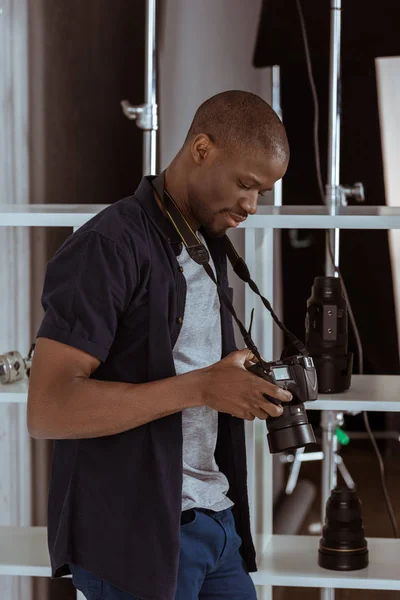 Side view of african american photographer choosing photos on photo camera in studio — Stock Photo