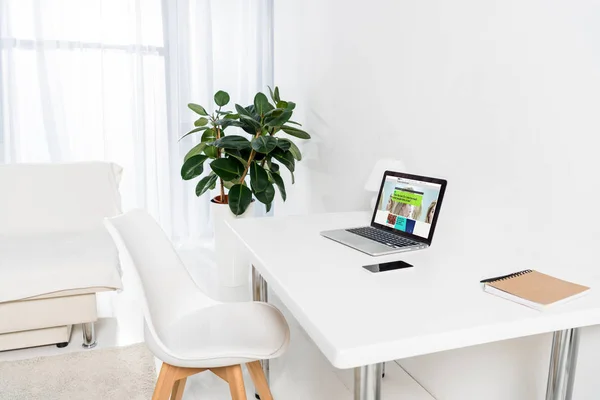 Oficina en casa con el ordenador portátil con el logotipo de la penes, teléfono inteligente y portátil en la mesa - foto de stock