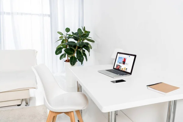 Laptop with ebay logo, smartphone and notebook on table in living room — Stock Photo