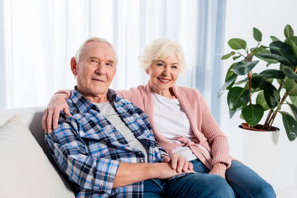 Porträt einer lächelnden älteren Frau und ihres Mannes, die in die Kamera schauen, während sie sich zu Hause auf dem Sofa ausruhen — Stockfoto