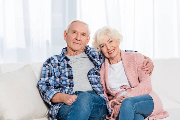 Ritratto di moglie e marito anziani sorridenti che guardano la macchina fotografica mentre riposano sul divano di casa — Foto stock