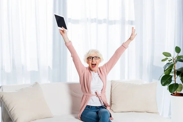 Retrato de mujer mayor excitada en gafas con la tableta en la mano mirando a la cámara en casa - foto de stock