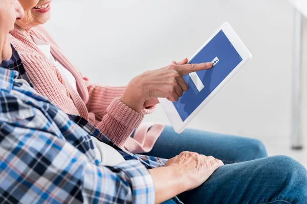 Tiro recortado de sorrir homem sênior e mulher usando tablet digital com logotipo do facebook na tela juntos — Fotografia de Stock