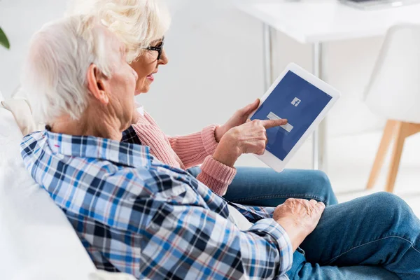 Side view of senior couple using digital tablet with facebook logo together — Stock Photo