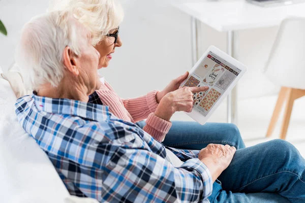 Seitenansicht eines älteren Paares, das zusammen ein digitales Tablet mit Pinterest-Logo benutzt — Stockfoto