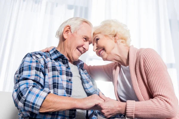 Vista de ángulo bajo de feliz pareja de ancianos mirándose el uno al otro y tomándose de la mano - foto de stock
