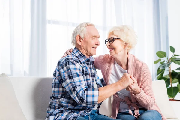 Feliz pareja de ancianos mirándose unos a otros y tomándose de la mano en casa - foto de stock