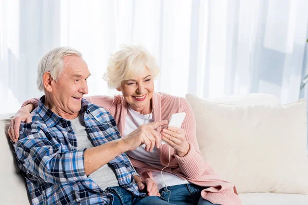 Glückliches Seniorenpaar mit Kopfhörern, das zu Hause gemeinsam Musik hört — Stockfoto