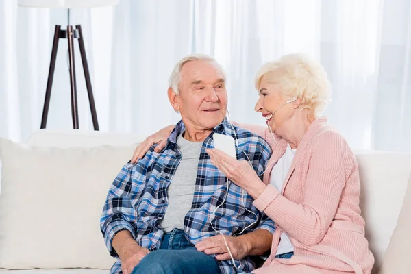 Glückliches Seniorenpaar mit Kopfhörern, das zu Hause gemeinsam Musik hört — Stockfoto