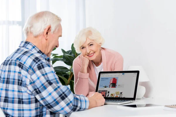 Portrait of senior woman looking at husband using laptop with ebay logo at home — Stock Photo