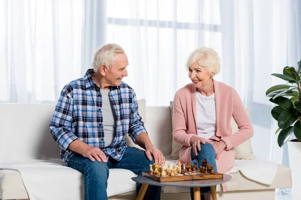 Couple aîné jouant aux échecs à la maison assis sur le canapé — Photo de stock