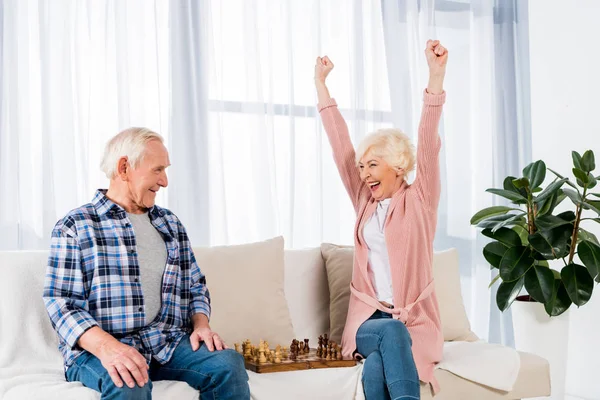 Happy senior couple playing chess at home on couch — Stock Photo