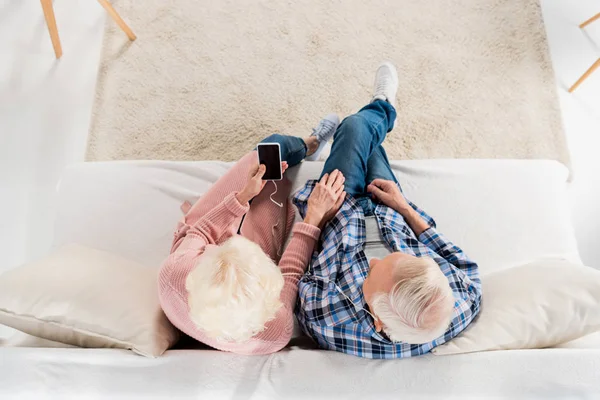 Vista aérea de pareja mayor escuchando música mientras está sentada en el sofá en casa - foto de stock