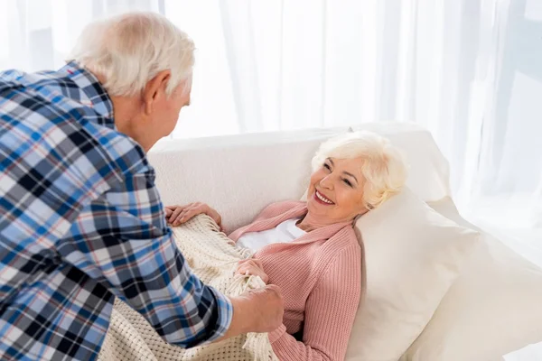 Senior homme couvrant femme heureuse avec couverture sur canapé confortable — Photo de stock