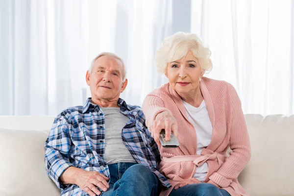 Casal sênior com controle remoto assistindo tv no sofá — Fotografia de Stock