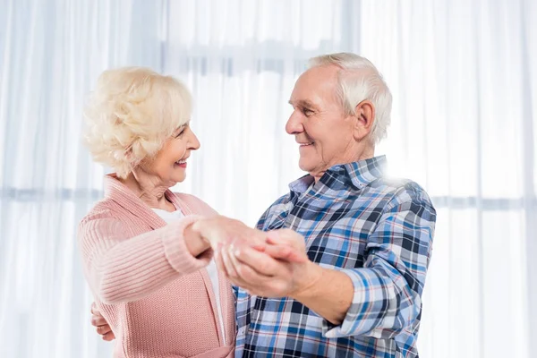 Vue latérale d'un couple de personnes âgées souriant dansant ensemble à la maison — Photo de stock