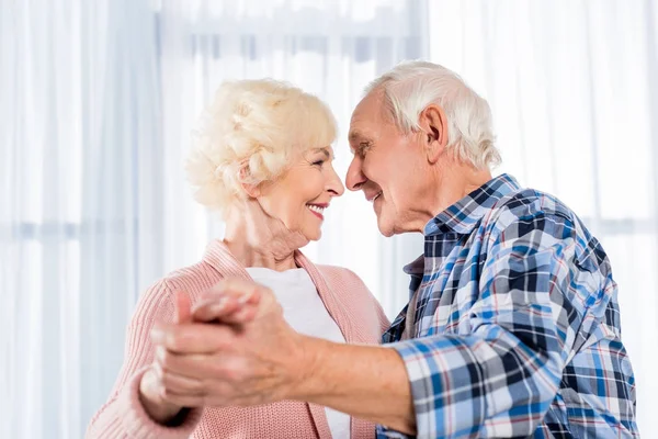 Vista lateral de la sonriente pareja de ancianos bailando juntos en casa - foto de stock