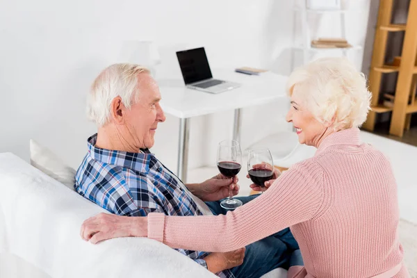 Rückansicht eines älteren Mannes und einer älteren Frau mit Rotweingläsern, die sich zu Hause anschauen — Stockfoto