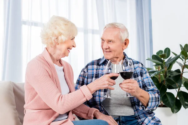 Retrato de casal sênior feliz copos clinking de vinho tinto enquanto descansa no sofá em casa — Fotografia de Stock