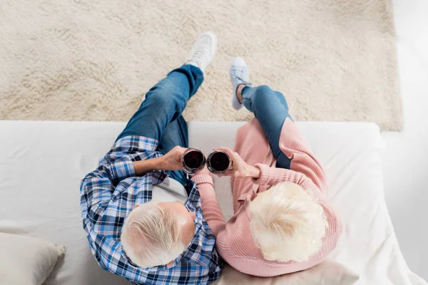 Vista aérea de pareja mayor con copas de vino tinto descansando en el sofá en casa - foto de stock