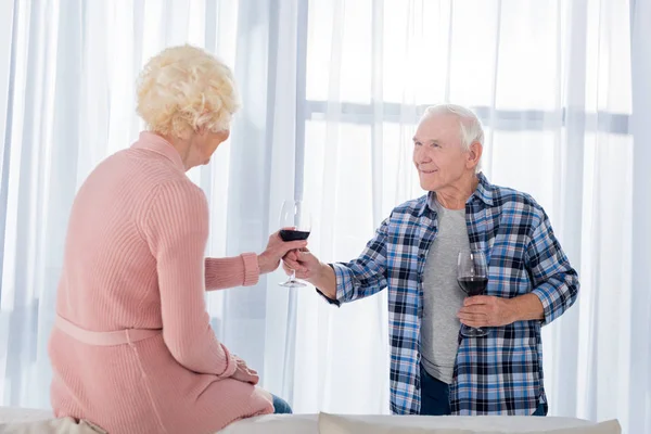 Seitenansicht eines älteren Mannes, der seiner Frau zu Hause ein Glas Rotwein schenkt — Stockfoto